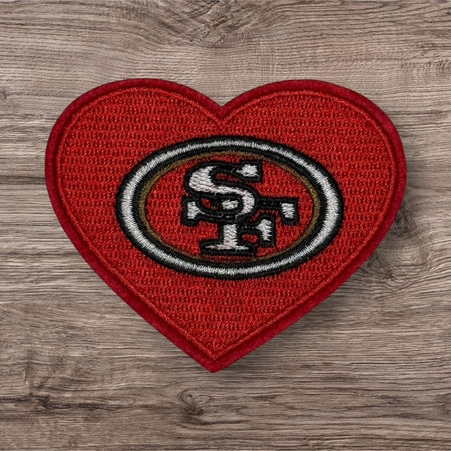 Red heart-shaped patch featuring San Francisco 49ers logo, embroidered fabric for sports fans.