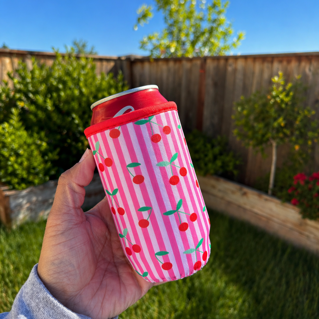 Hand holding a can with a pink cherry-patterned sleeve outdoors.