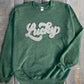 A green crewneck sweatshirt with the word 'Lucky' written in a cursive chenille patch on the front.