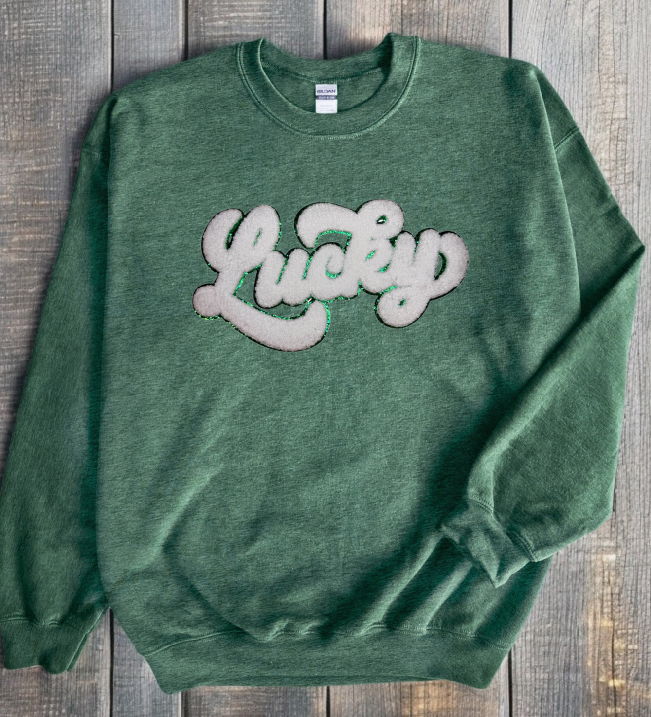 A green crewneck sweatshirt with the word 'Lucky' written in a cursive chenille patch on the front.