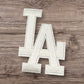 White LA letter patch, textured fabric, perfect for customizations and personalizing clothing items.